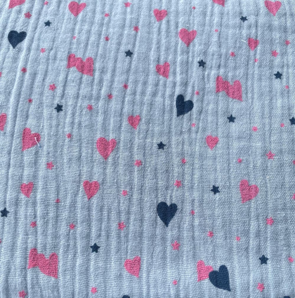 Weicher Musselin-Stoff in hellem Graublau, bedruckt mit rosa Herzen und dunkelblauen Sternen. Klassische Double-Gauze Baumwollqualität mit Crinkle-Optik für Kinderzimmer-Deko und Kleidung