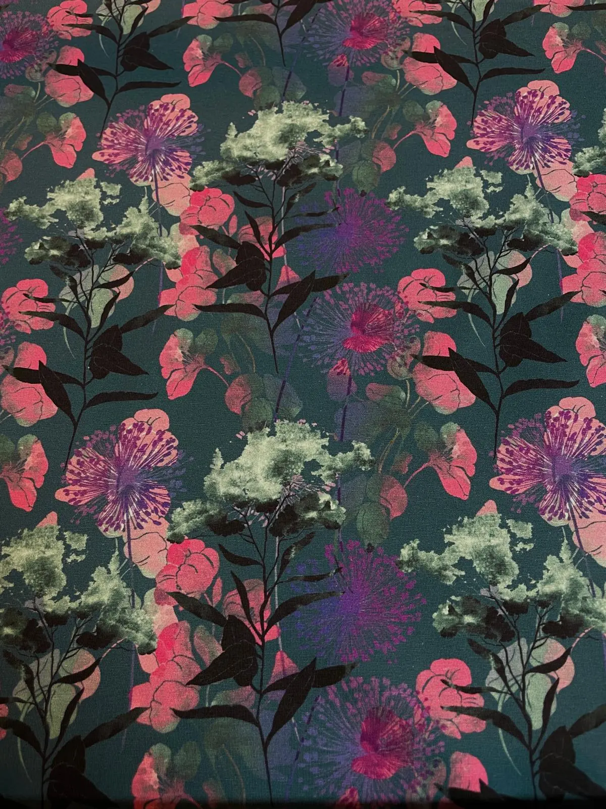 Hochwertiger Jersey-Stoff mit einem dichten, floralen Muster aus Wildblumen und Gräsern. Das Design zeigt verschiedene Blütenformen in kräftigem Pink, Beere und Hellgrün auf einem tiefen, dunkelgrünen Hintergrund. Ideal für herbstliche und elegante Damenb
