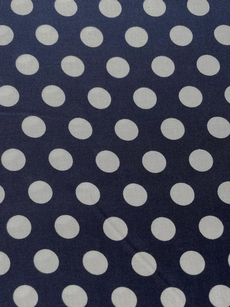 Nahaufnahme eines fließenden, dunkelblauen Viskosestoffs mit einem regelmäßigen Muster aus großen, hellbeigen Polka Dots. Die Stoffbreite beträgt 142cm.
