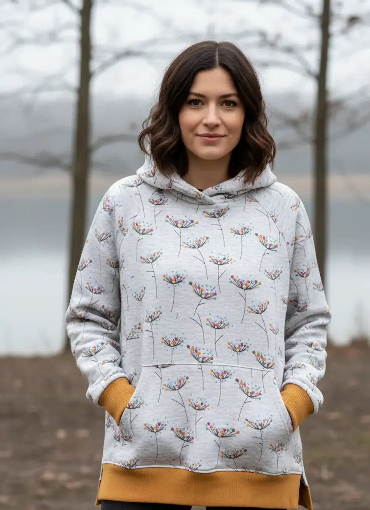 Ein selbstgenähter Baby-Kuschelanzug mit Füßen aus hellgrau meliertem Alpenfleece mit Doldenblüten-Muster, kombiniert mit senfgelben Bündchen, flach ausgebreitet auf einer Strickdecke.