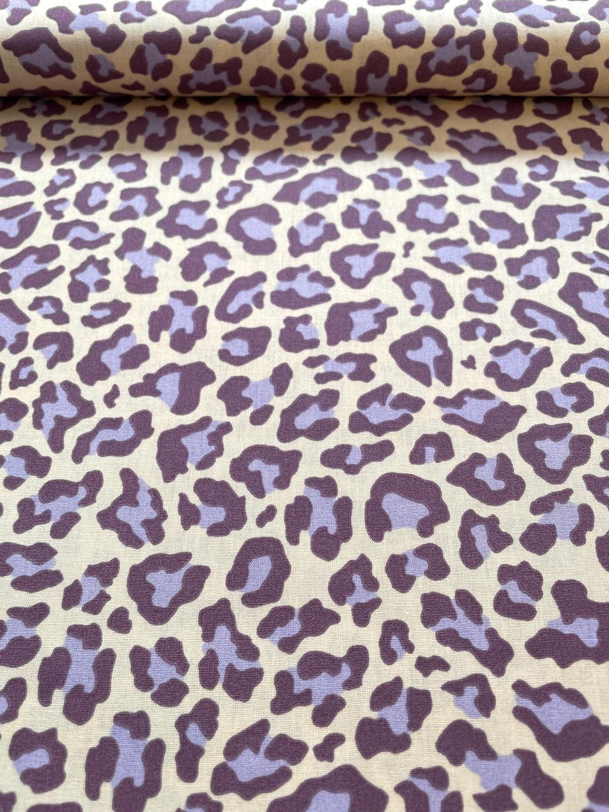 Hochwertiger Baumwollstoff mit modernem Leopardenmuster in Flieder und dunklem Lila auf hellem Hintergrund.