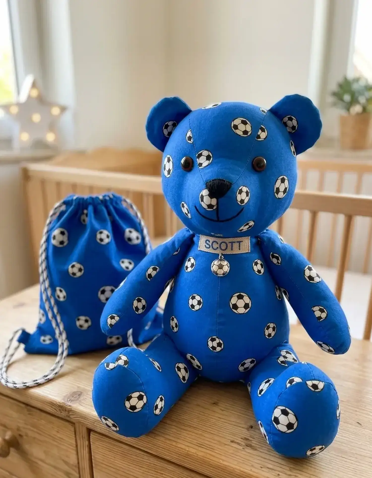 Ein handgemachter Stoffbär mit dem Namen „Scott“ und ein passender Turnbeutel, genäht aus royalblauem Baumwollstoff mit Fußball-Muster als Dekoration im Kinderzimmer.