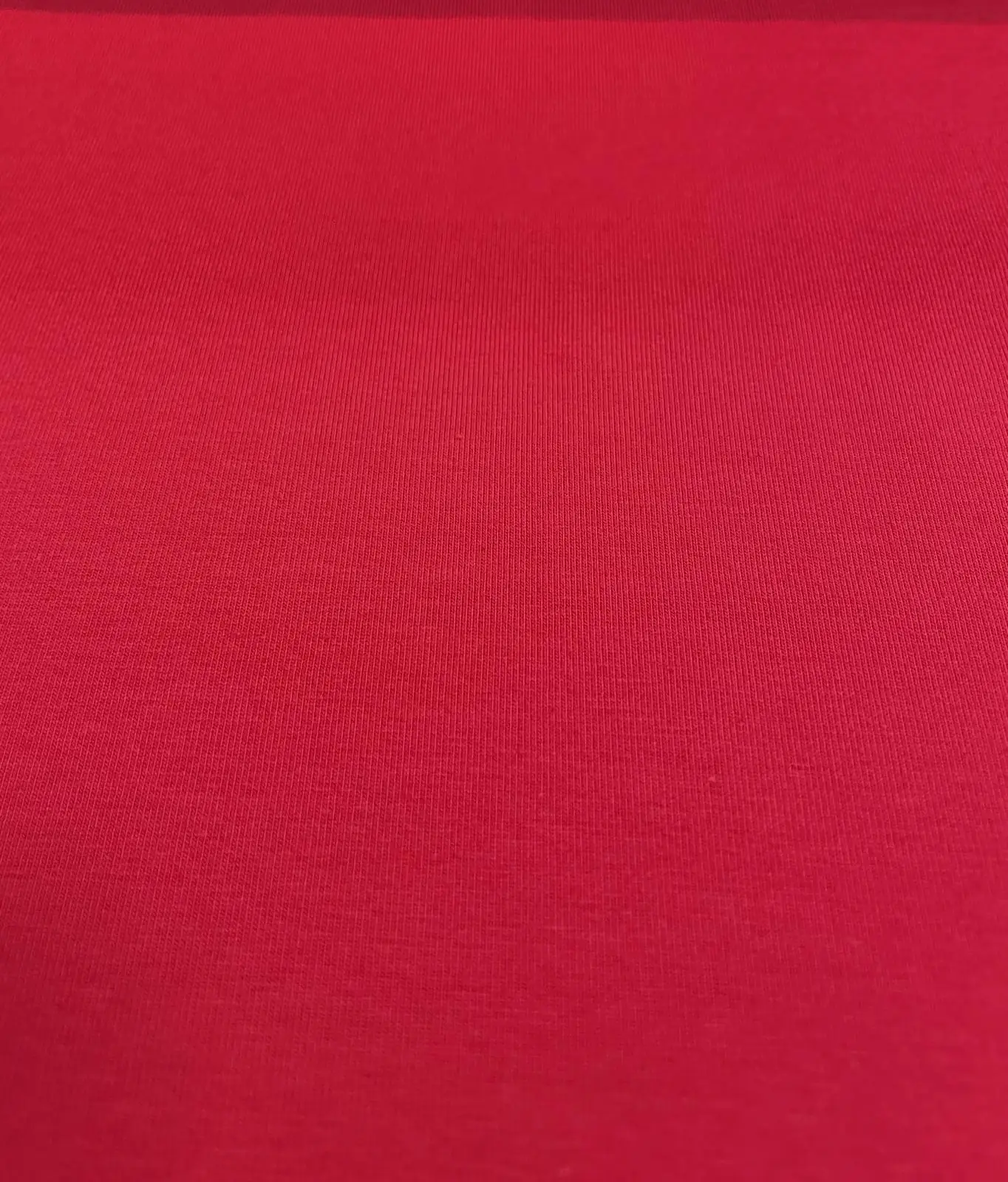 Eine detailreiche Nahaufnahme von einem unifarbenen, kräftig roten Baumwolljersey-Stoff als Meterware mit einer glatten, gleichmäßigen Oberflächenstruktur.