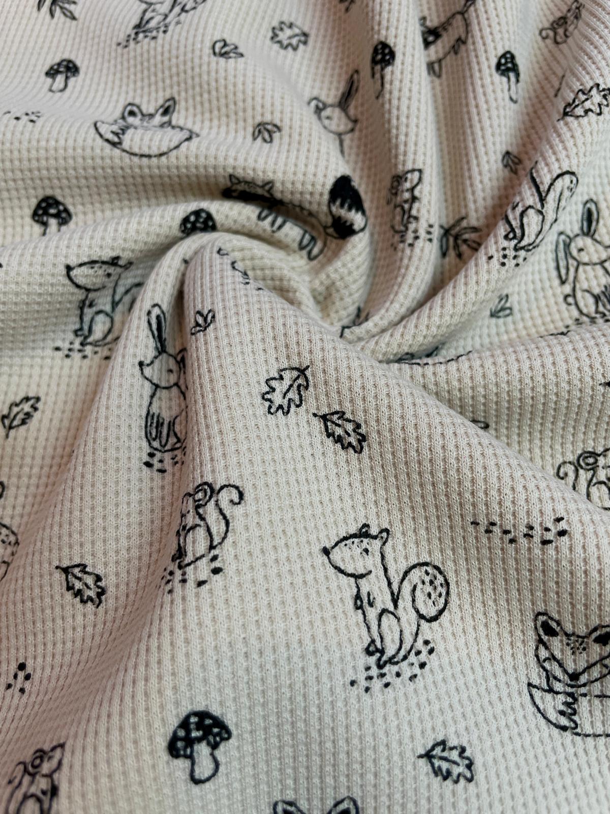 Strukturierter Waffeljersey Stoff als Meterware in Beige mit einem feinen, schwarz-weißen Muster aus Waldtieren wie Füchsen, Eichhörnchen, Waschbären und Pilzen.