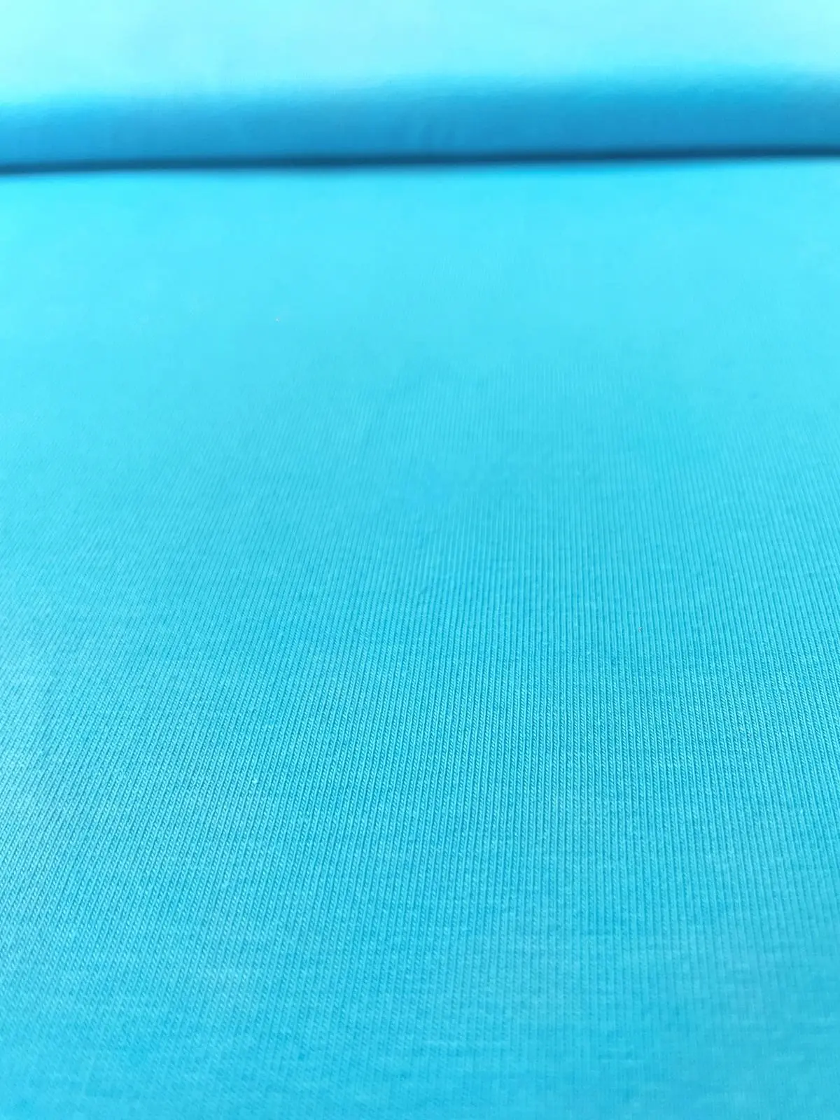 Nahaufnahme von elastischem Baumwolljersey in leuchtendem Türkis, glatte Oberfläche, 215g Gewicht, 144cm breite Meterware.