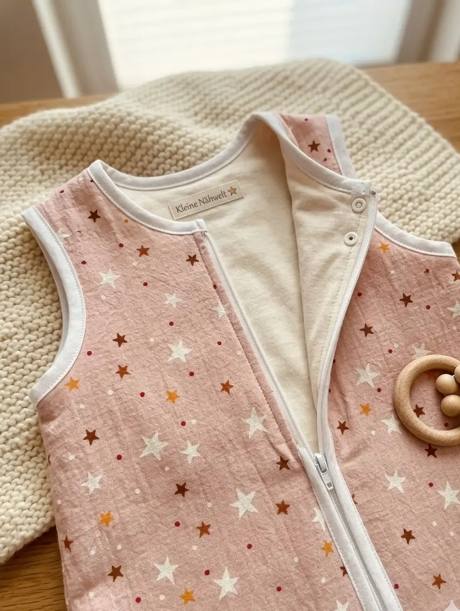 Detailansicht eines handgefertigten Babyschlafsacks aus apricotfarbener Kochbaumwolle mit Sternenmuster, weißem Reißverschluss und dem Label „Kleine Nähwelt“.