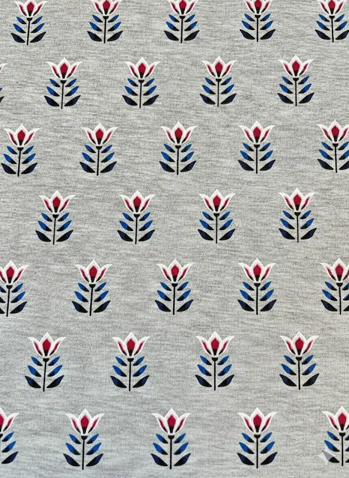 Hochwertiger Baumwolljersey als Meterware in Grau-Meliert, bedruckt mit einem regelmäßigen, geometrischen Retro-Muster aus rot-weißen Tulpen und dunkelblauen Blättern. Ideal für Bekleidung wie Shirts, Kleider und Kinderkleidung.