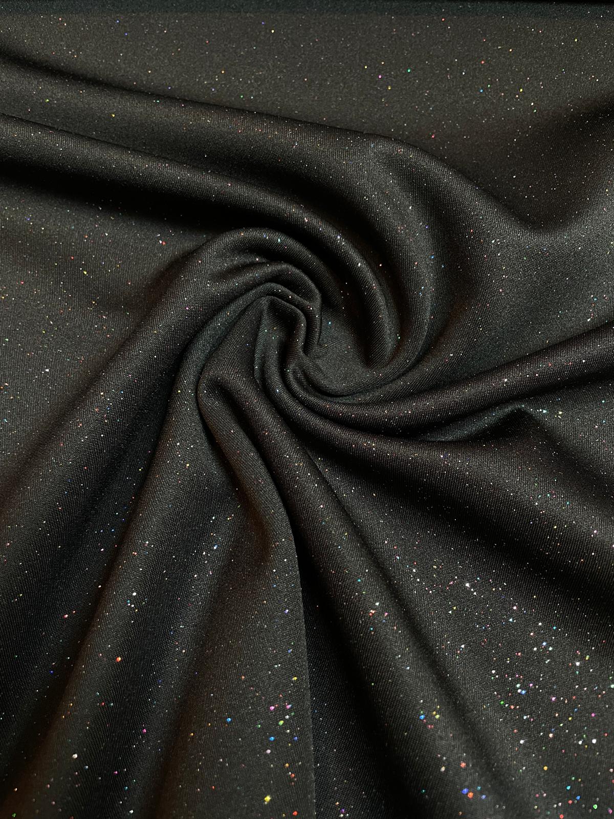 Nahaufnahme eines schwarzen Jerseystoffs, der mit vielen kleinen, bunten Glitzerpunkten (Multicolor) übersät ist und im Licht funkelt.