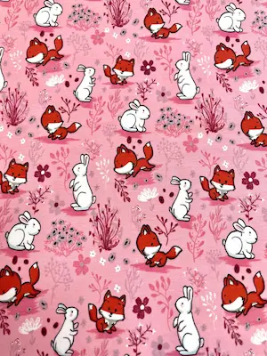 Niedlicher Baumwolljersey in Rosa mit kleinen Füchsen, weißen Hasen und floralen Elementen wie Blumen und Gräsern, perfekt für Baby- und Kinderkleidung.