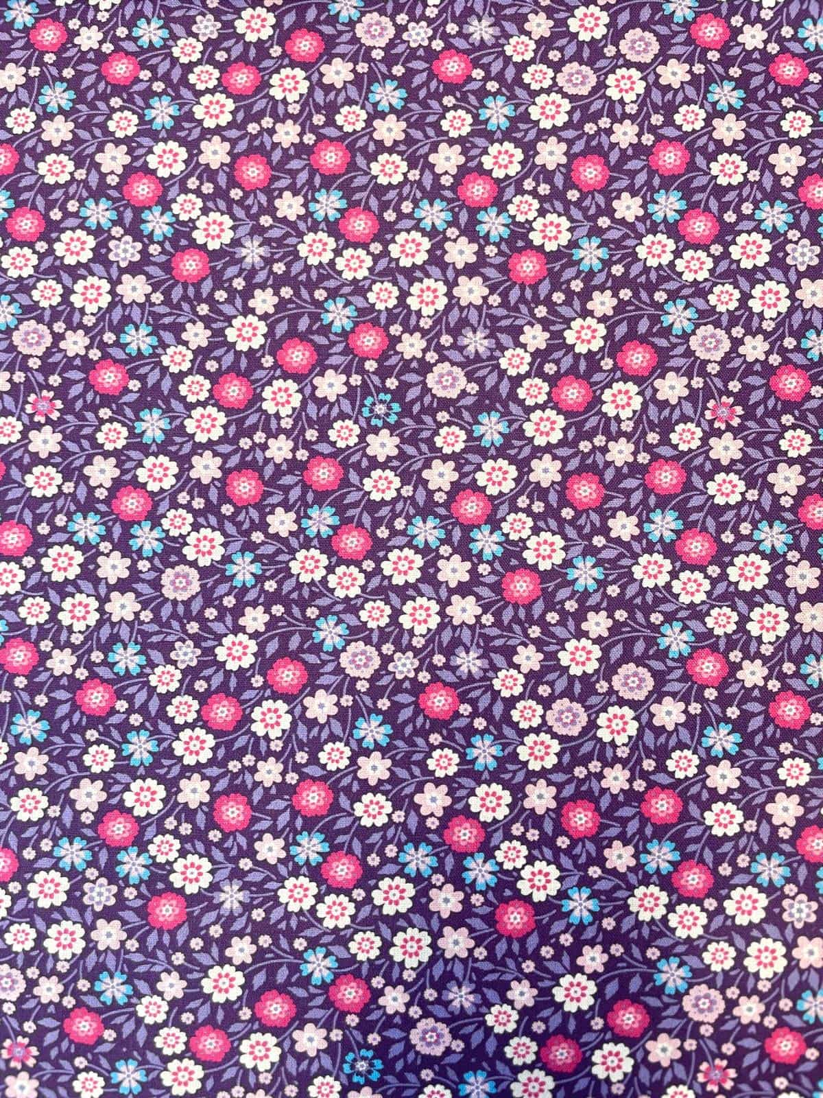 Nahaufnahme einer violetten Baumwoll-Webware mit einem dichten Muster aus kleinen rosa, pinken und hellblauen Streublumen und feinen Blattranken.