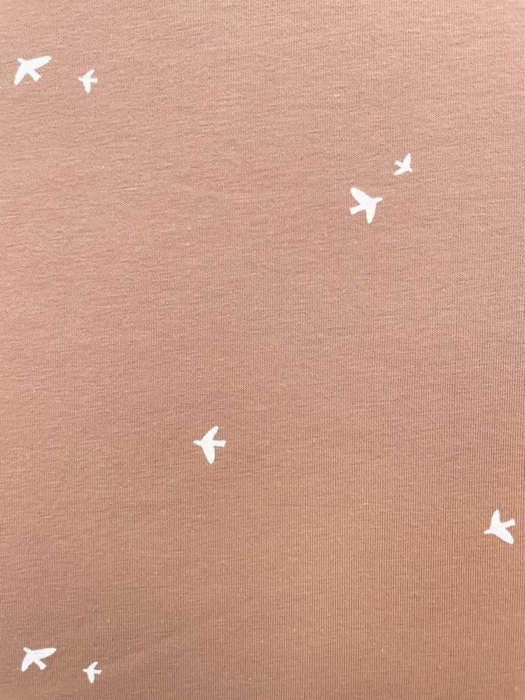 Elastischer Baumwolljersey in der Farbe Terracotta mit einem Muster aus kleinen, weißen Vögeln.