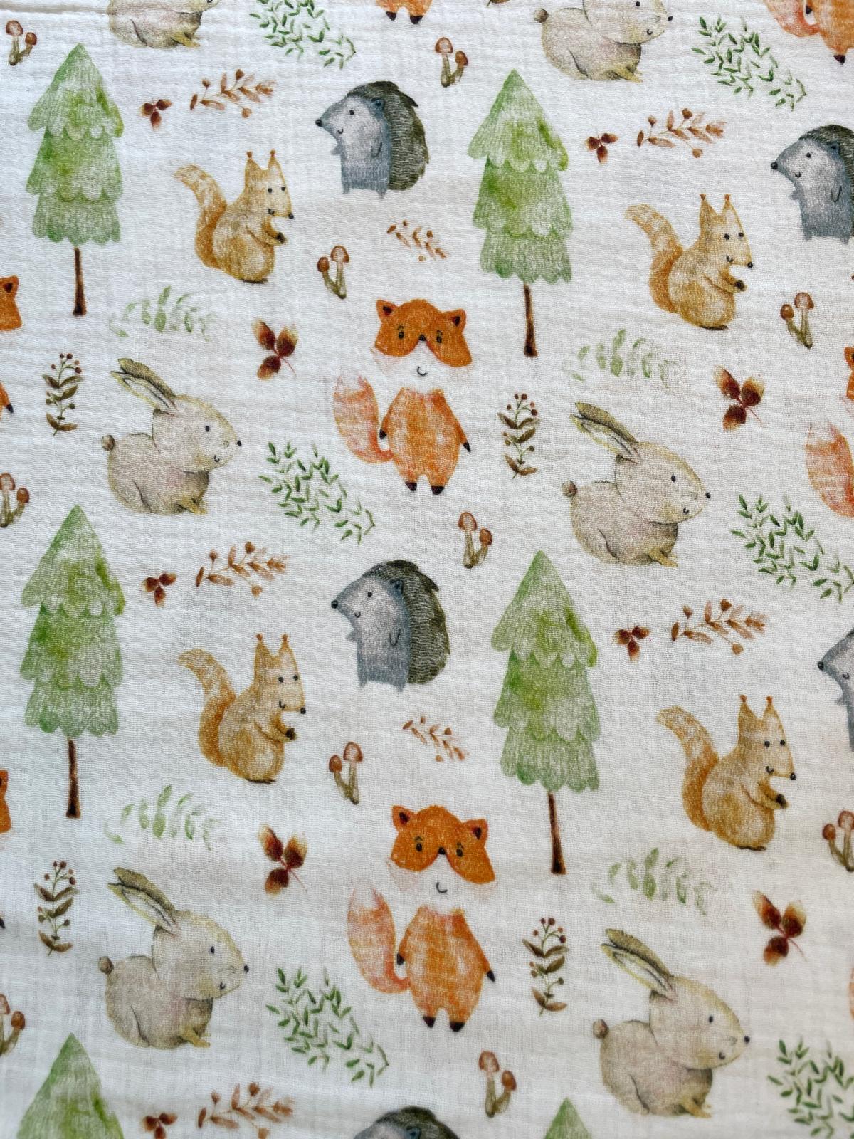 Cremefarbener Musselinstoff mit buntem Waldtiere-Print bestehend aus Fuchs, Eichhörnchen, Hase, Igel, Tannen und Pilzen. 100% Baumwolle, Double-Gauze Qualität.