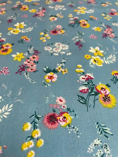Hellblaue beschichtete Baumwolle mit bunten Blumenwiesen-Print (gelbe, rosa und weiße Blüten), wasserabweisende Meterware