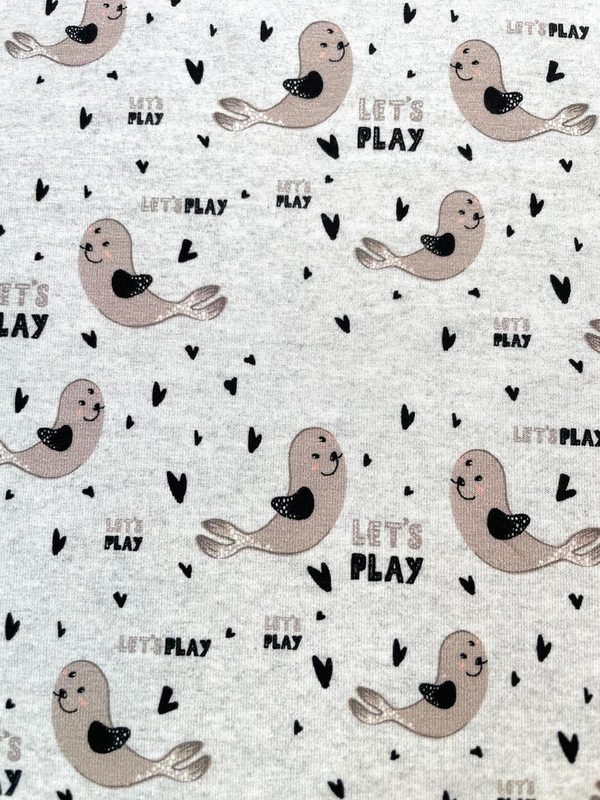 Hellgrau melierter Baumwolljersey als Meterware für Babys, bedruckt mit kleinen beigen Seehunden, schwarzen Herzen und dem Schriftzug Let's Play.