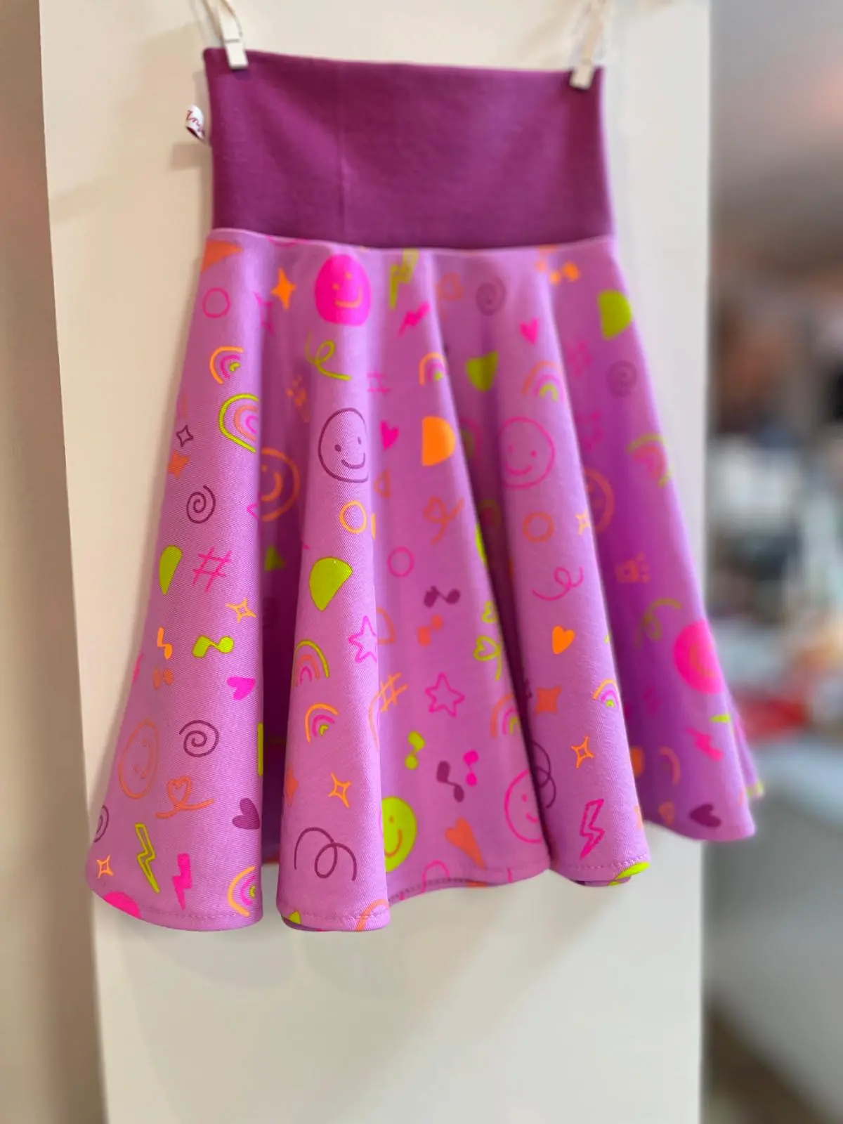 Handgemachter Mädchenrock aus fliederfarbenem Jersey mit bunten Neon-Smileys und Doodle-Motiven. Ausgestellter Schnitt mit breitem, kontrastfarbenem Komfortbündchen in Beere.