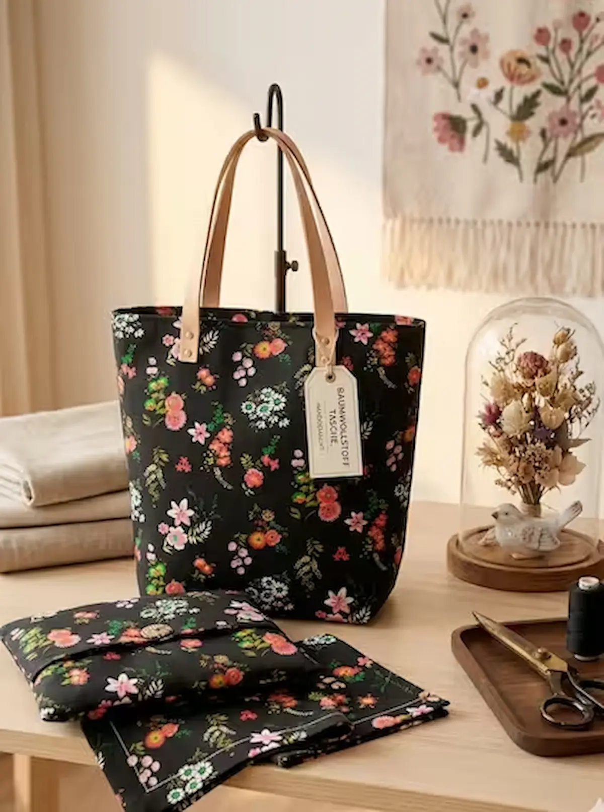 Hochwertiger Baumwoll-Popeline-Stoff als Meterware in Schwarz mit farbenfrohem floralem Wiesenblumenmuster, genäht als elegante Handtasche mit Lederhenkeln auf einem Studiotisch.