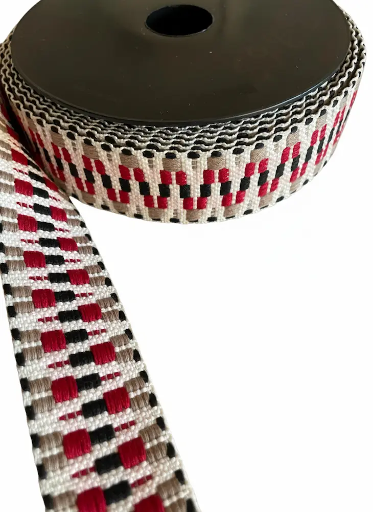 Gewebtes Gurtband mit 38mm Breite auf schwarzer Spule, geometrisches Muster in Rot, Schwarz, Grau und Creme als Meterware für Taschengurte
