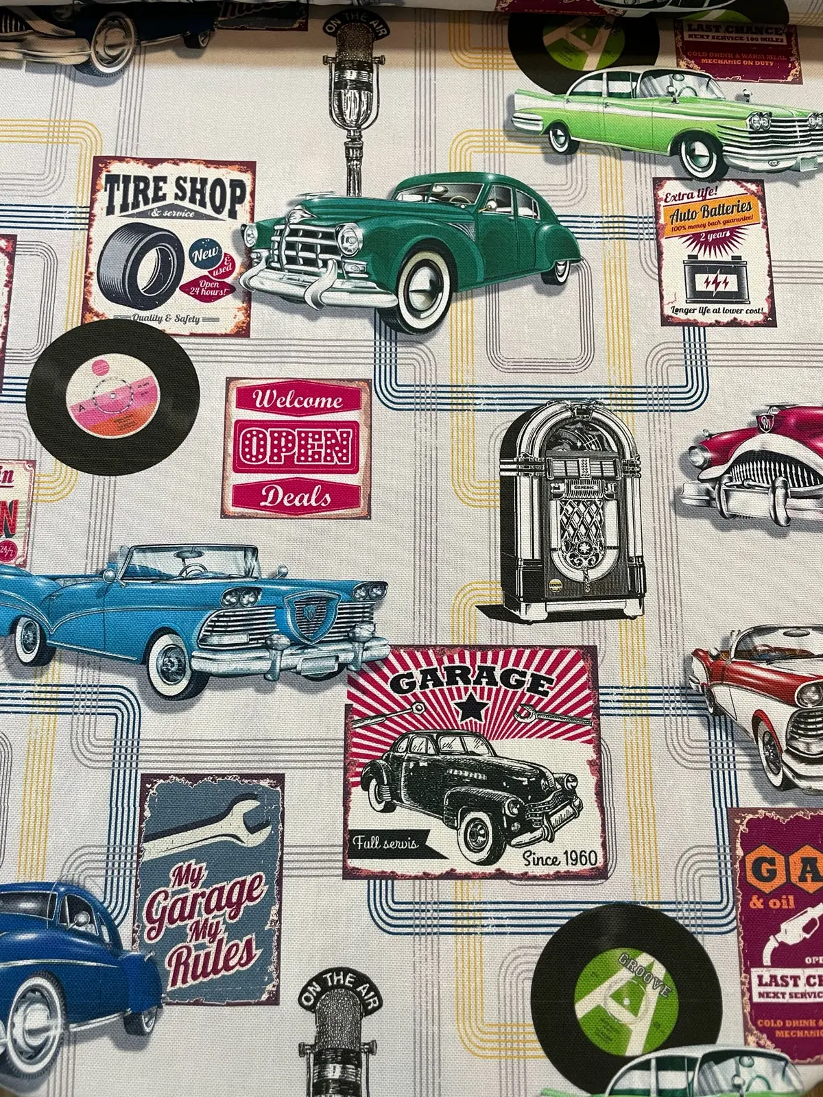 Farbenfroher Dekostoff als Meterware im Vintage-Stil mit klassischen Oldtimern, Jukeboxen, Schallplatten und amerikanischen Werkstatt-Schildern.