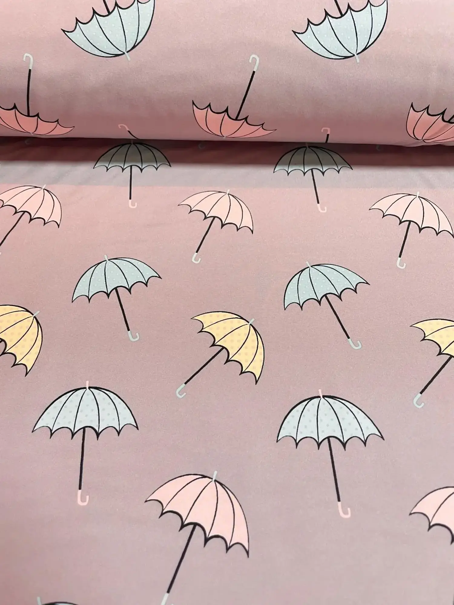 Outdoor-Softshell-Stoff in Altrosa, bedruckt mit filigranen Regenschirmen in Pastelltönen wie Hellblau, zartem Gelb und Rosa. Die Regenschirme haben schwarze Griffe und dezente Pünktlich-Muster. Hochwertiger Funktionsstoff für Mädchenjacken und Regenbekle