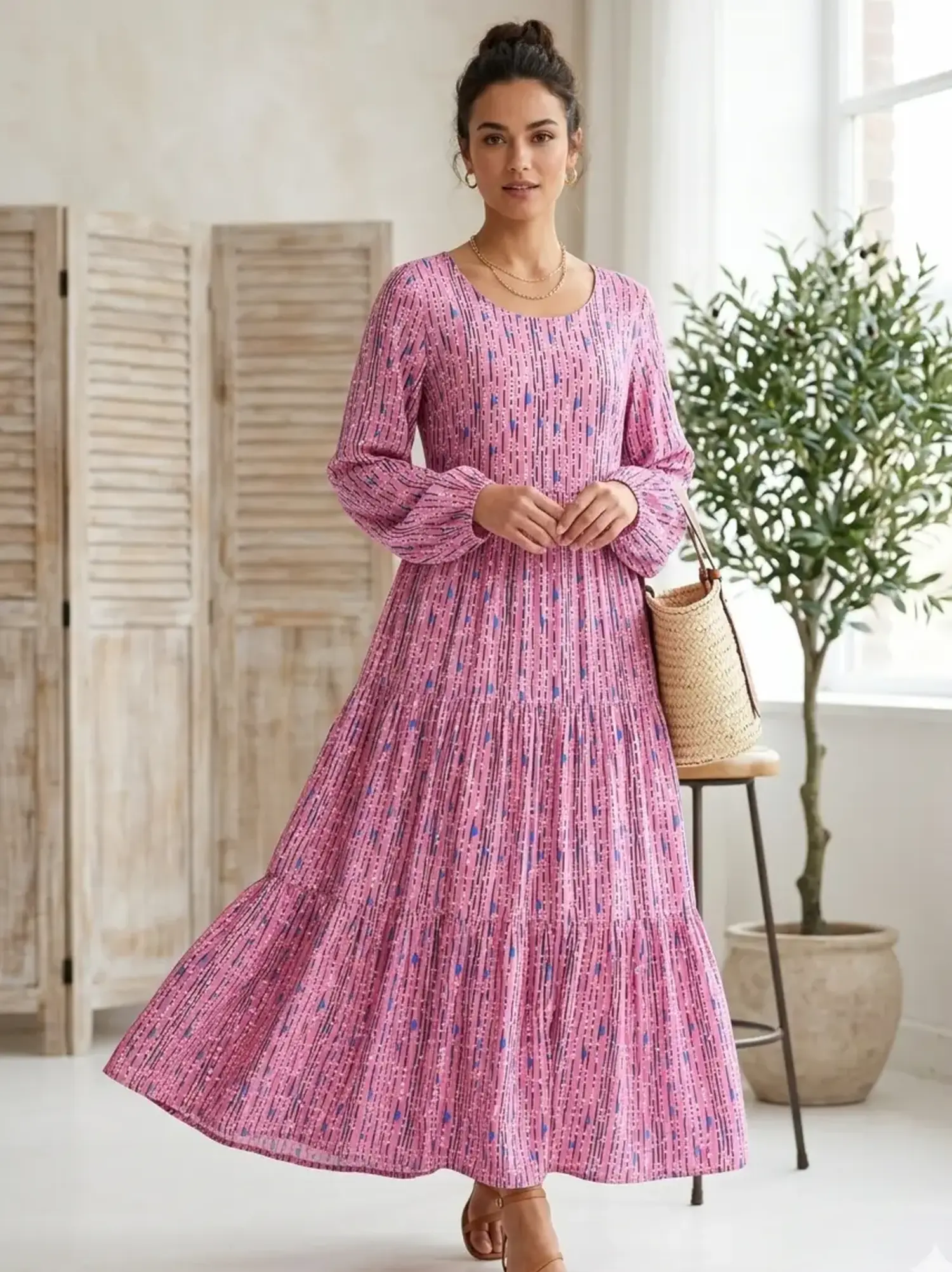 Elegantes gestuftes Maxikleid aus weich fließender Viskose Webware mit grafischem Muster in Rosa und Blau, getragen von einer Frau in hellem Interieur.