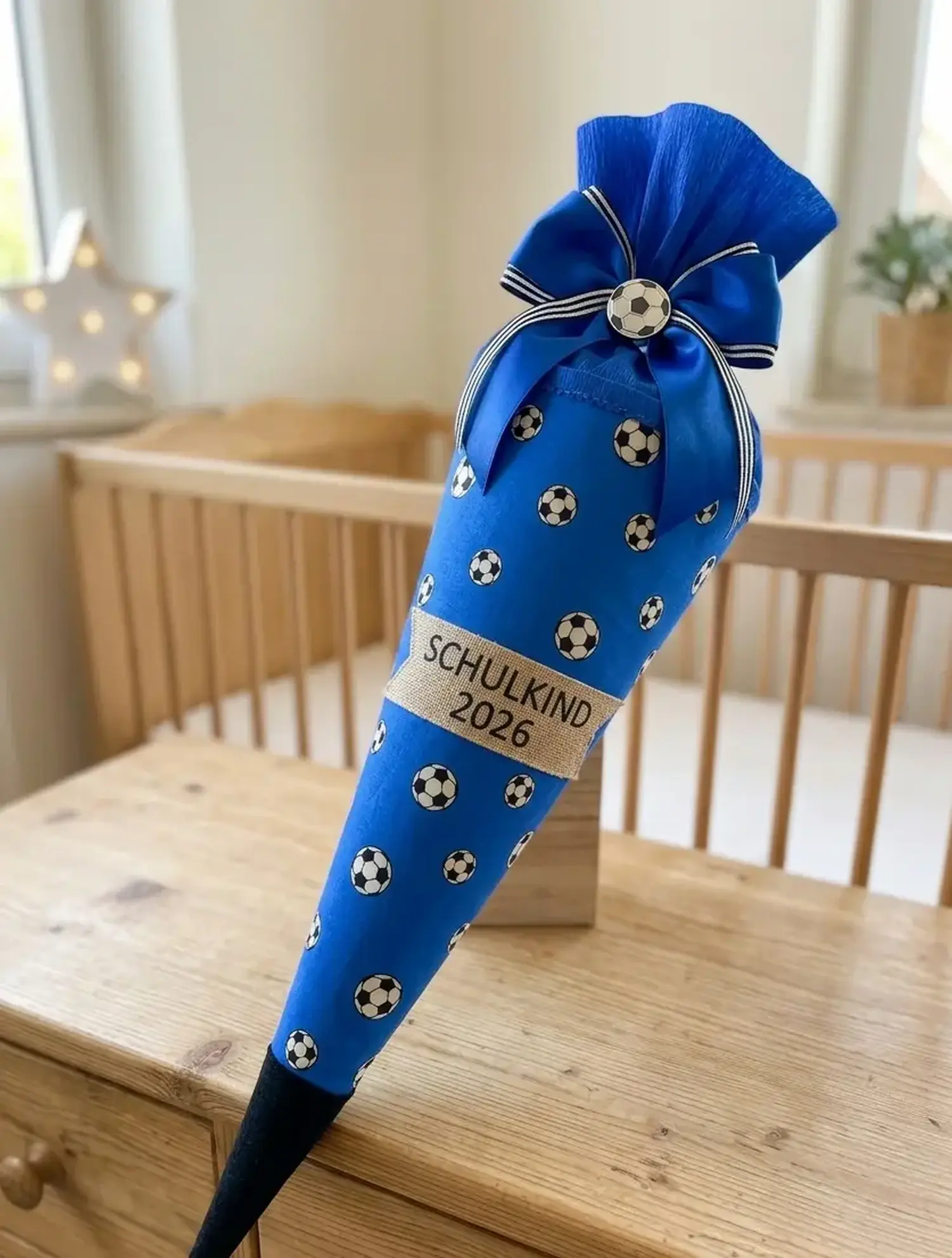 Eine handgemachte Schultüte zur Einschulung aus royalblauem Baumwollstoff mit Fußball-Muster, verziert mit einer blauen Schleife und einem Juteband mit der Aufschrift „Schulkind 2026“.