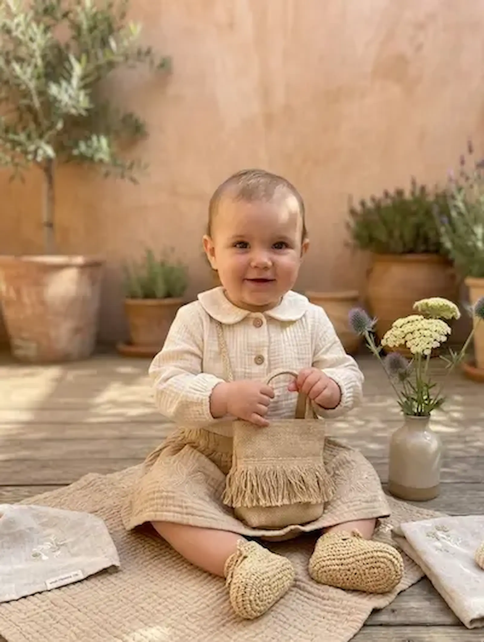 Baby in einer Bluse aus beigem Musselin Stoff, sitzend auf einer Musselindecke, Anwendungsbeispiel für Double Gauze Meterware in Uni Beige.
