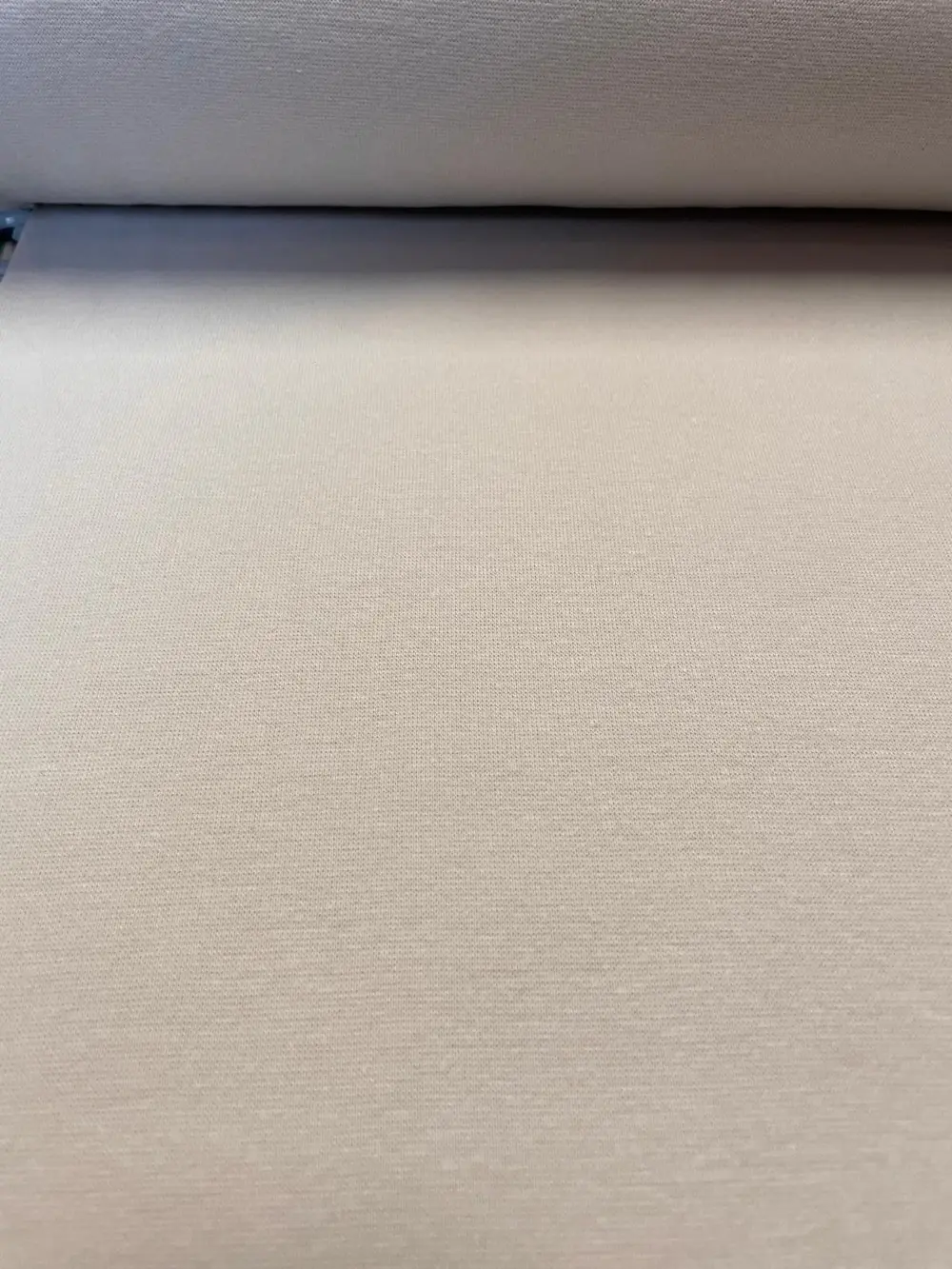 Nahaufnahme von elastischem Bündchenstoff in hellem Grau-Beige (Greige) als Meterware für Kleidung und Abschlüsse.