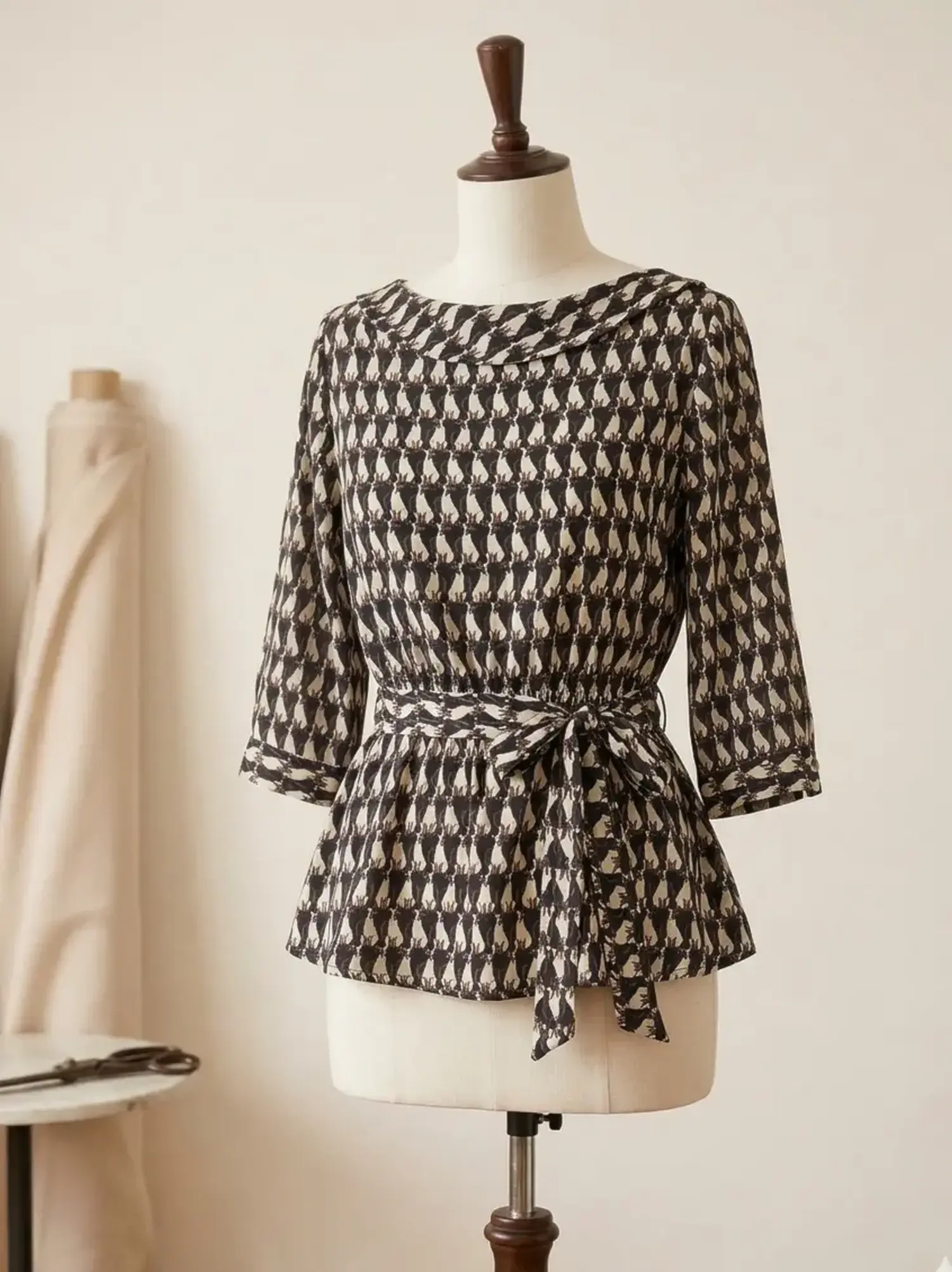 Elegante Schößchen-Bluse aus Viskose Webware mit dezentem Katzen-Muster in Schwarz und Beige auf einer Schneiderpuppe in einem Nähatelier.