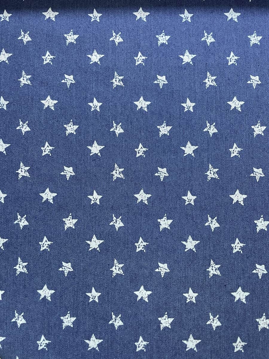 Blauer Jeansstoff als Meterware, bedruckt mit einem gleichmäßigen Muster aus kleinen, weißen Sternen im Used-Look.