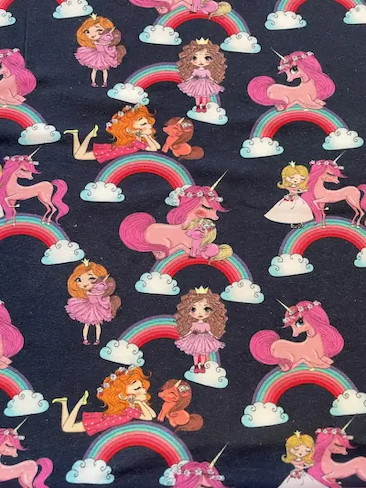 Elastischer Jersey-Stoff in Dunkelblau mit einem fortlaufenden Muster für Kinder. Zu sehen sind rosa Einhörner, bunte Regenbögen mit weißen Wolken sowie kleine Prinzessinnen in rosa Kleidern und Kronen. Perfekter Baumwolljersey für farbenfrohe Kinderkleid