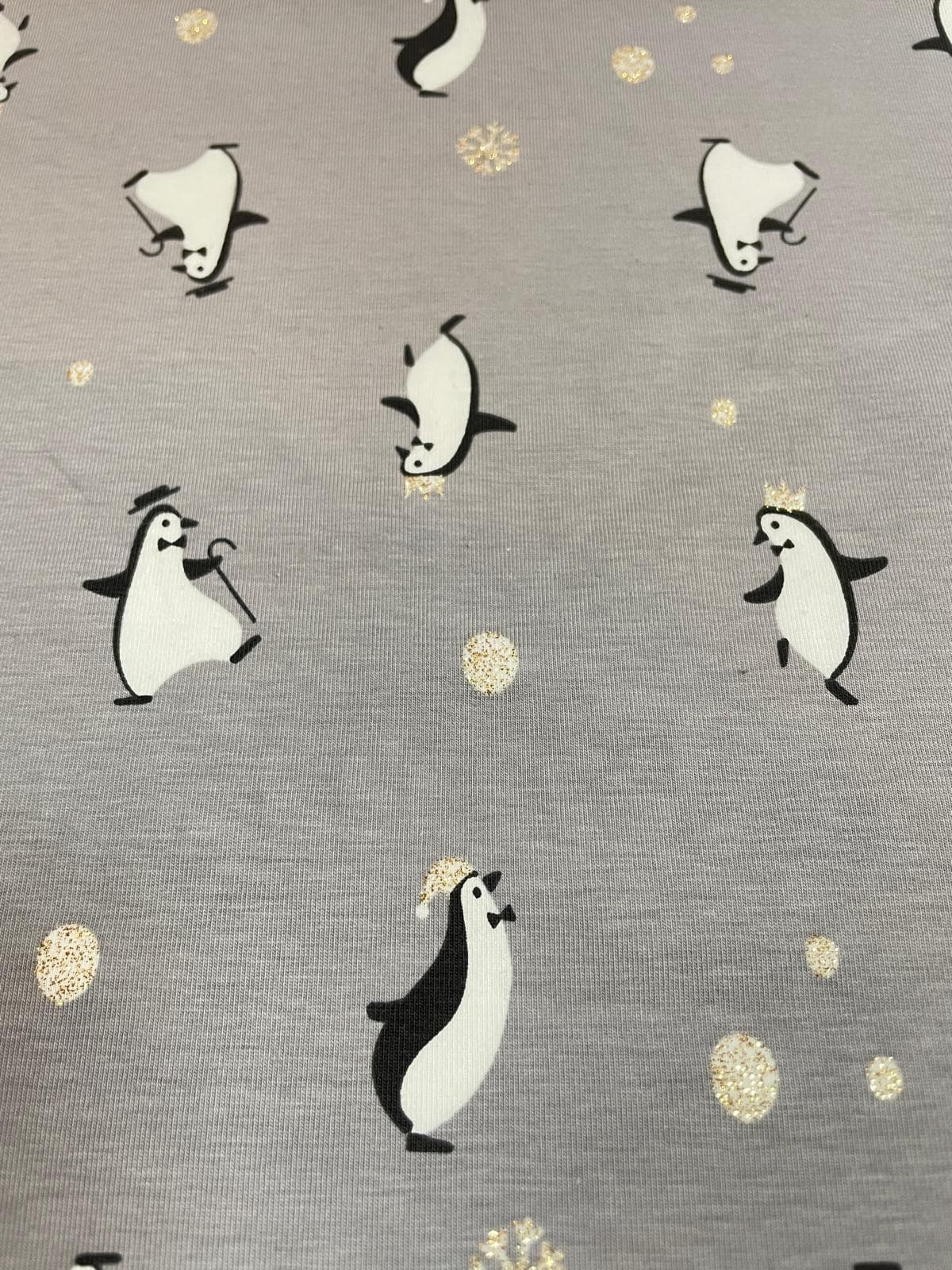 Grauer Baumwoll-Jersey als Meterware mit niedlichen Pinguinen, teils mit Hüten oder Kronen, sowie funkelnden Glitzer-Schneeflocken und Punkten.