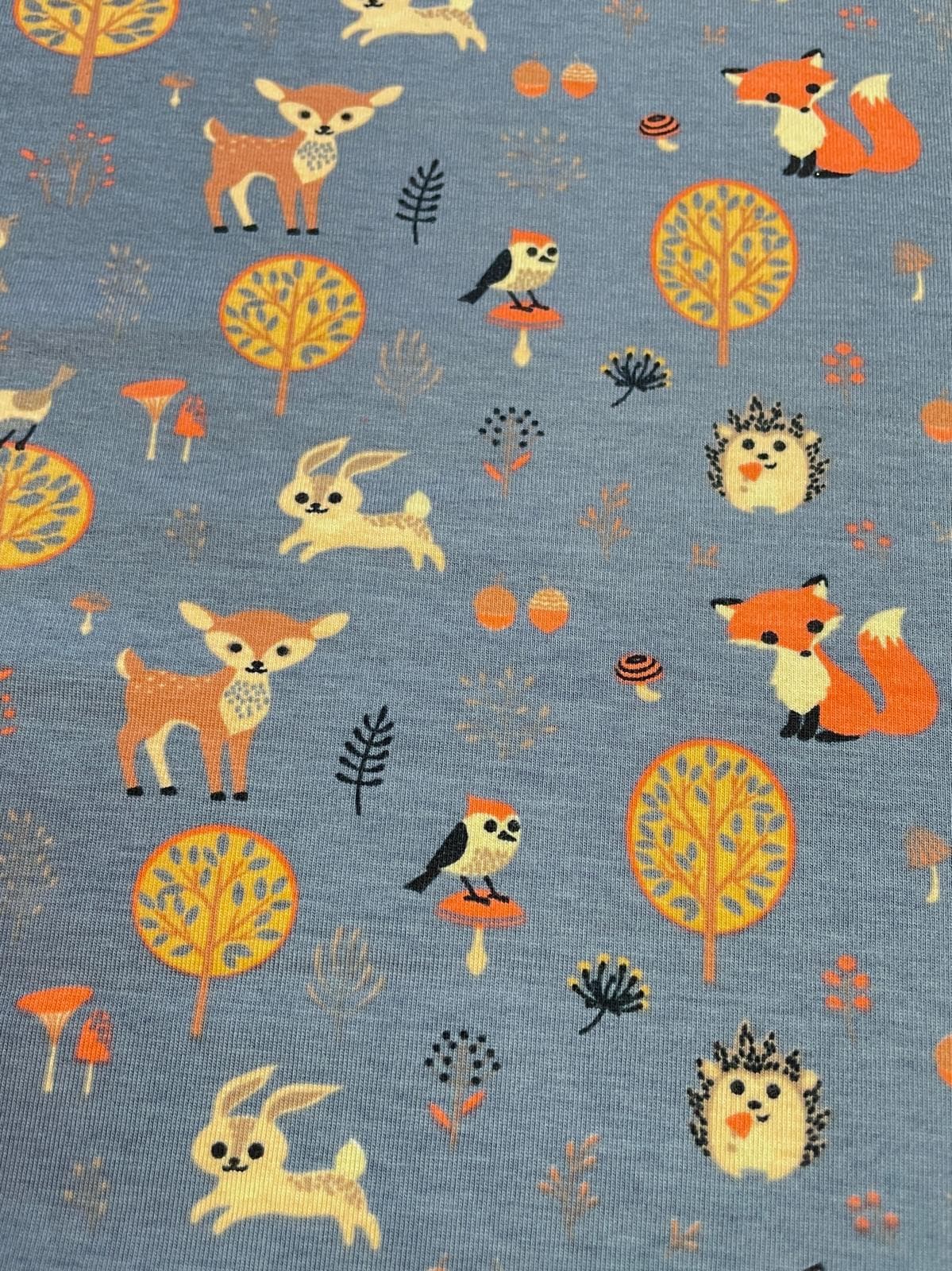 Farbenfroher Baumwolljersey in Jeansblau meliert, bedruckt mit niedlichen Waldtieren wie Fuchs, Reh, Igel und Hase sowie bunten Bäumen und Pilzen.