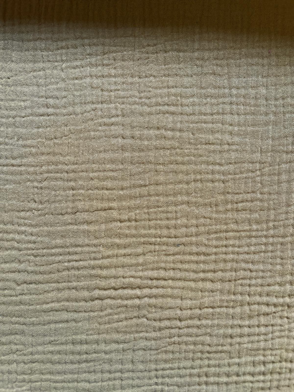 Nahaufnahme von beige-farbenem Musselin-Stoff aus 100% Baumwolle mit charakteristischer Crinkle-Struktur für Babykleidung.