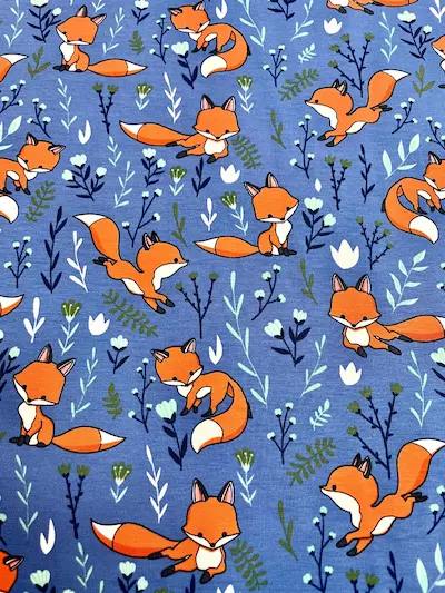 Hochwertiger Baumwolljersey in kräftigem Blau mit verschiedenen Fuchs-Motiven und kleinen floralen Elementen wie Farnen und Blüten, ideal für Kinder-Shirts und Babykleidung.