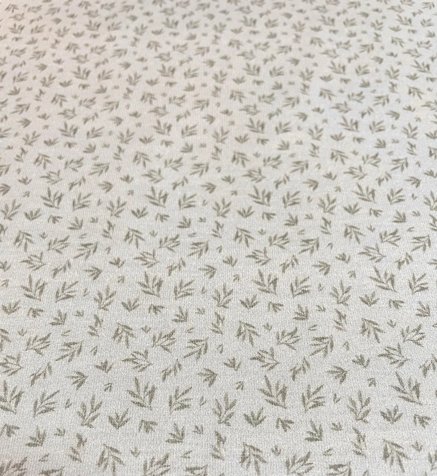 Hellbeiger Jersey-Stoff mit einem feinen, minimalistischen Muster aus kleinen graubraunen Blättern. Die gleichmäßige Anordnung der grafischen Zweige auf dem hellen Untergrund wirkt ruhig und modern, ideal für zeitlose Basic-Kleidung.