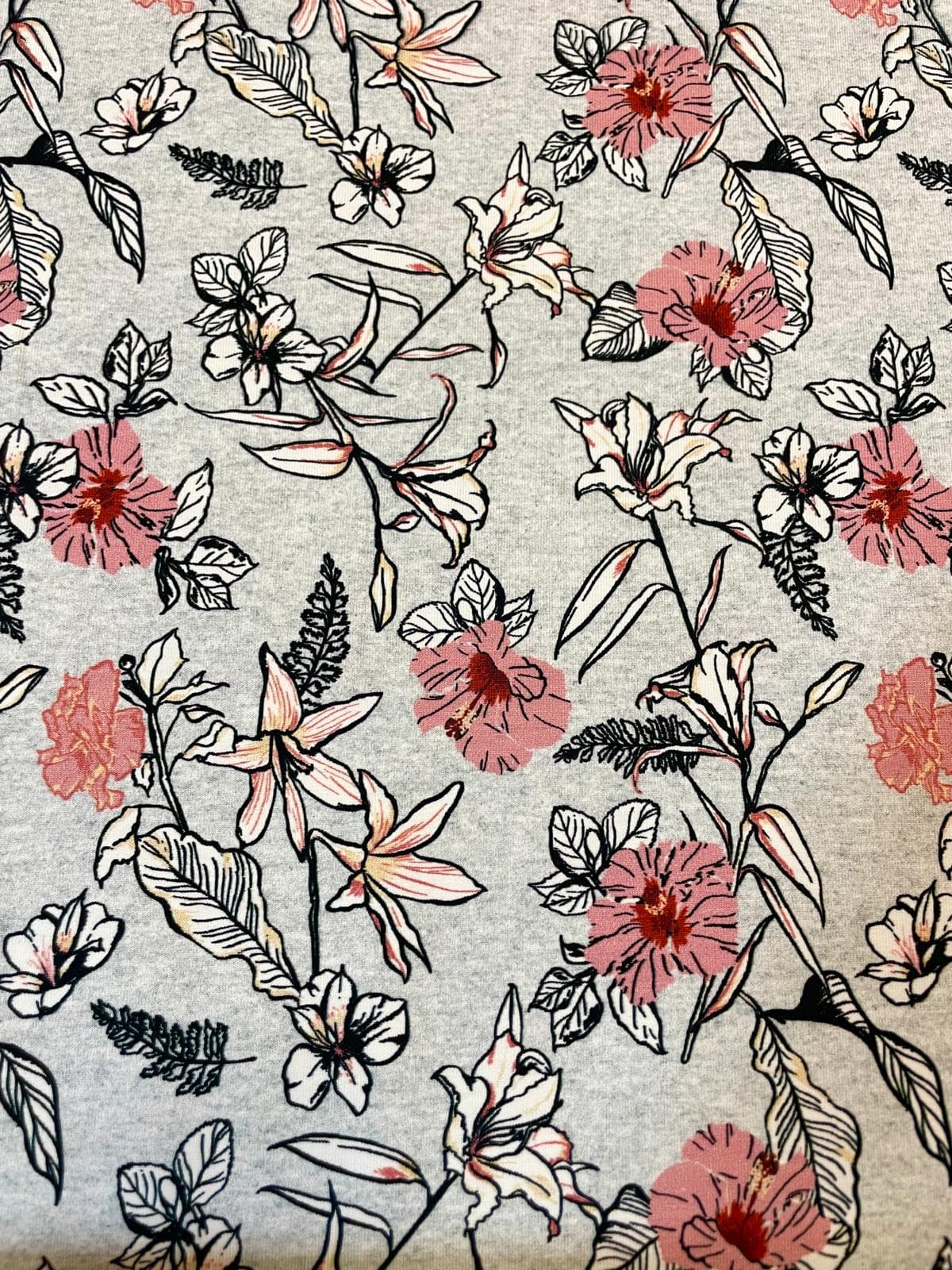 Weicher Baumwolljersey-Stoff als Meterware mit floralem Print aus rosa-roten Hibiskusblüten und Lilien mit schwarzen Konturen auf grau-melierte Hintergrund.