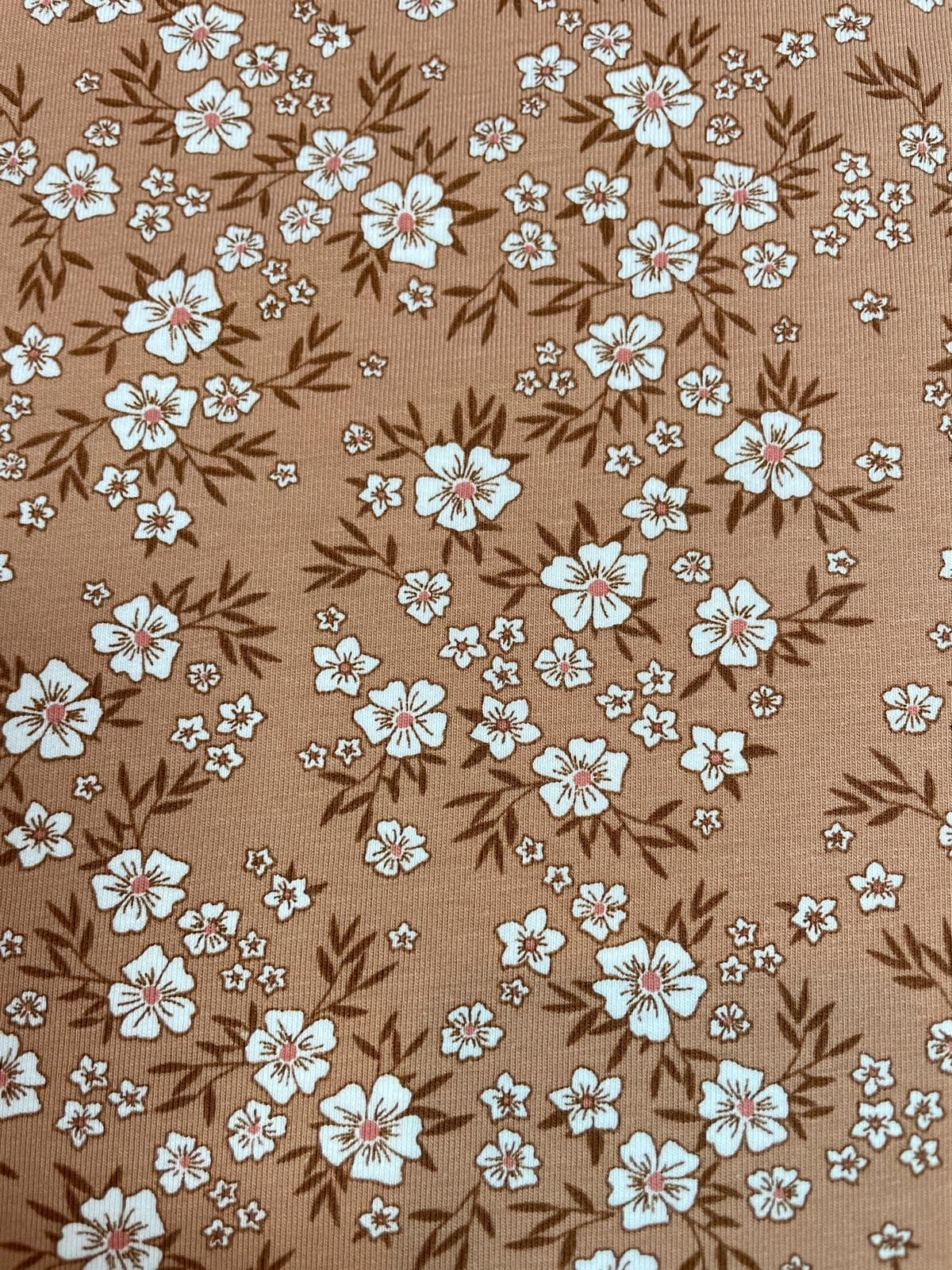 Weicher Jerseystoff in Ocker mit dichten weißen Wiesenblumen, elastische Baumwoll-Meterware für herbstliche Kinder- und Damenmode.