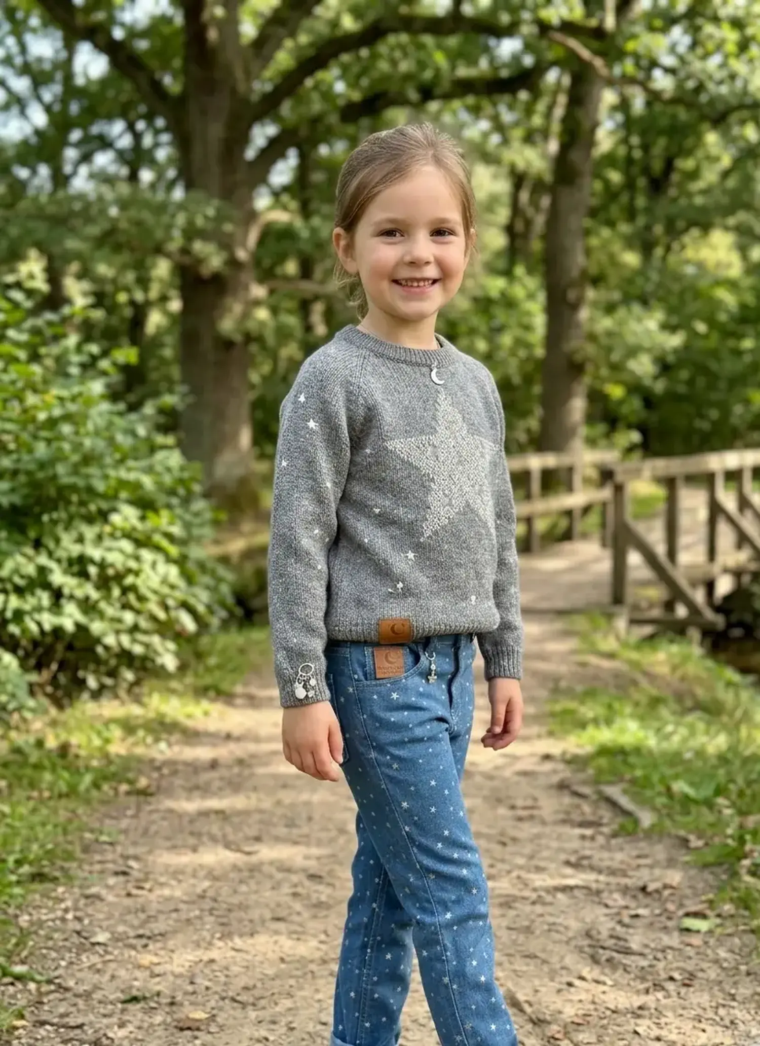 Kleines Mädchen trägt eine Hose aus leichtem, blauem Jeansstoff mit kleinen silbernen Sternen bedruckt.