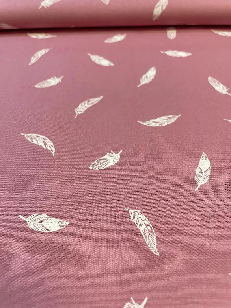 Hochwertiger Webware-Baumwollstoff als Meterware in einem matten Altrosa oder staubigen Roséton. Der Stoff zeigt ein dezentes, elegantes Allover-Muster aus filigran gezeichneten, weißen Federn, die unregelmäßig über die feine Gewebestruktur verteilt sind.