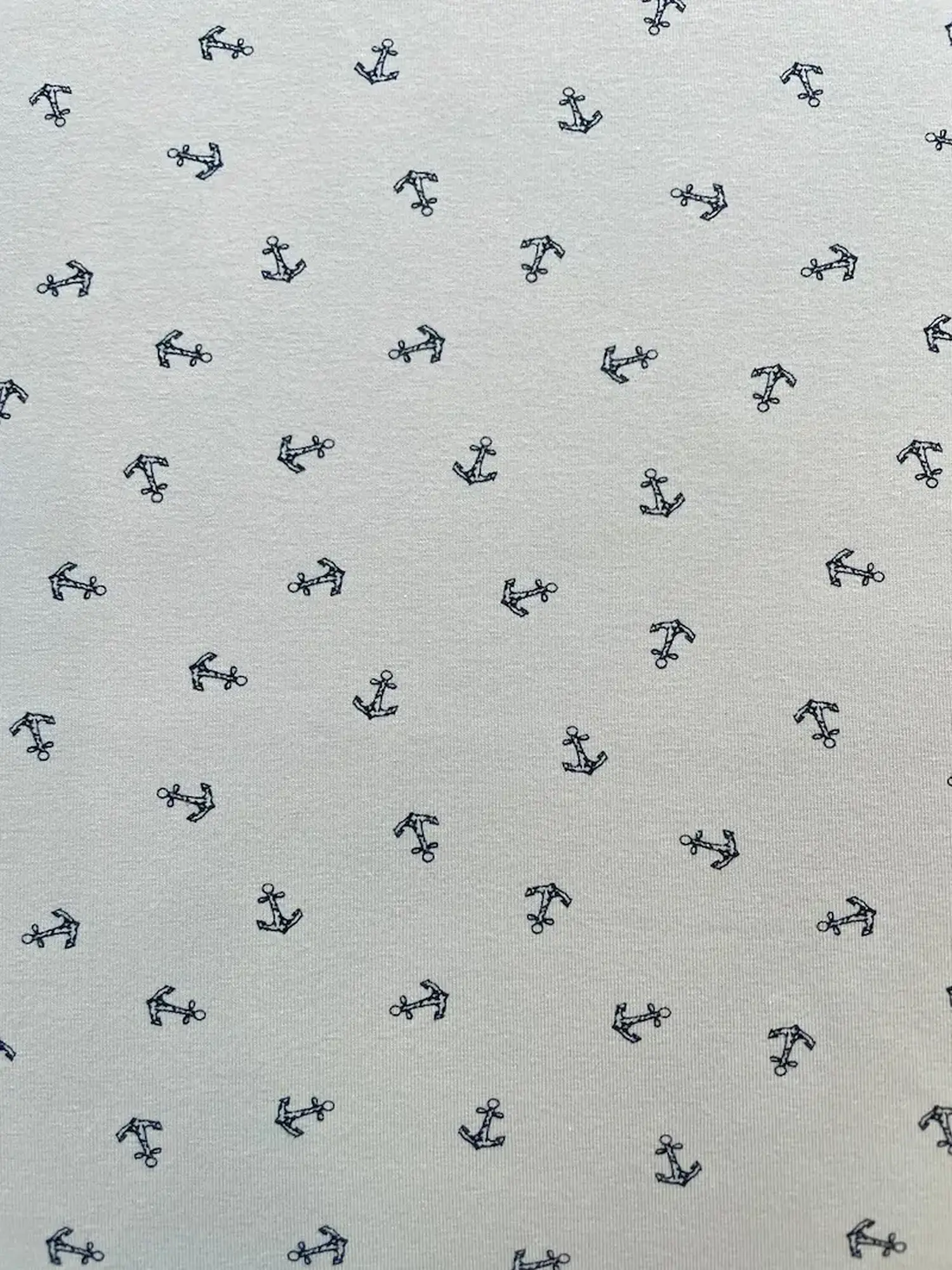 Nahaufnahme eines hellgrauen Baumwolljersey-Stoffes mit kleinen, dunkelblauen Ankern als Allover-Print. Ideale elastische Meterware für maritime Nähprojekte.