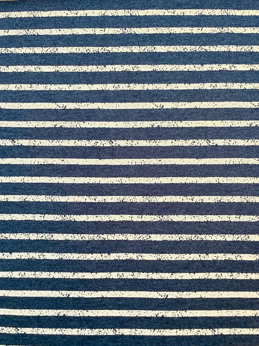 Nahaufnahme von Baumwolljersey Meterware mit horizontalen Streifen in Dunkelblau und Weiß; die hellen Streifen weisen eine leicht unregelmäßige Vintage-Optik auf; ideal für maritime Kleidung und elastische Nähprojekte.