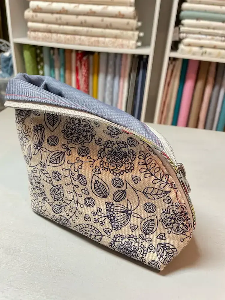 Eine handgemachte Kosmetiktasche mit Reißverschluss, genäht aus festem Canvas-Dekostoff mit blauem Mandala-Blumenmuster auf beigem Grund.