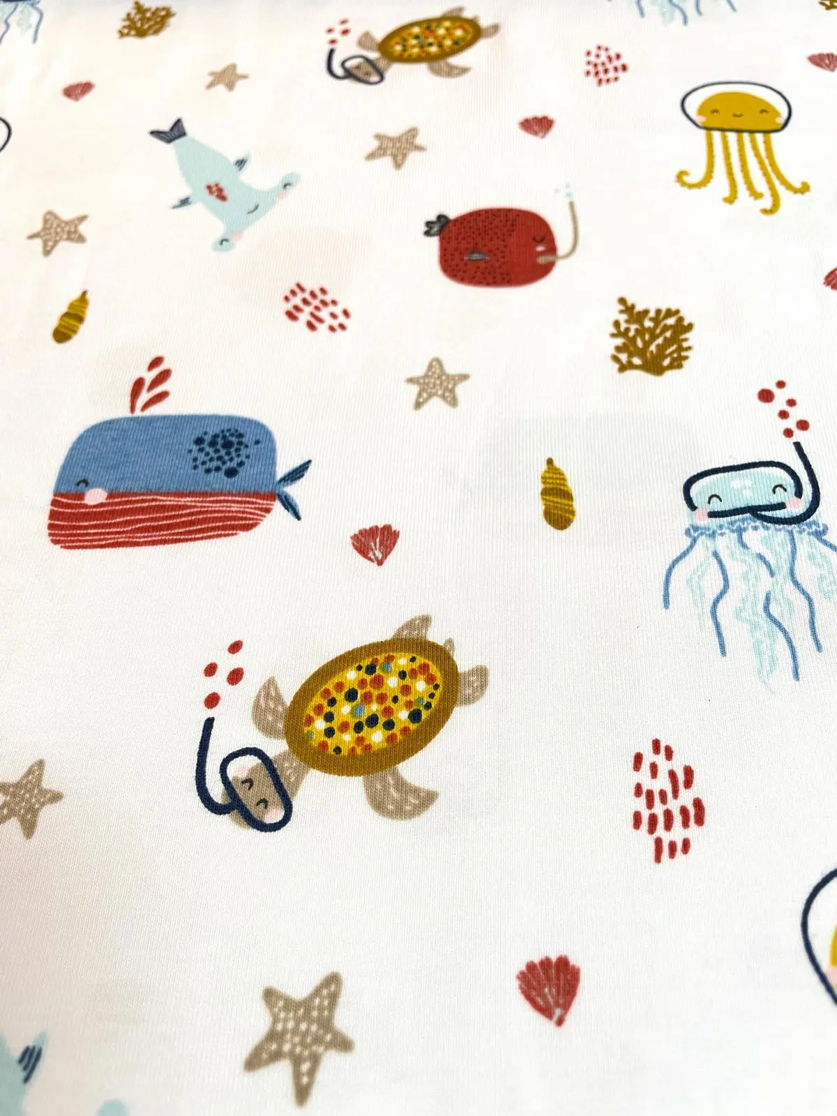 Weißer Jersey-Stoff mit bunten Meeresbewohnern wie Walen, Schildkröten mit Schnorchel, Quallen und Seesternen im kindgerechten Illustration-Stil.