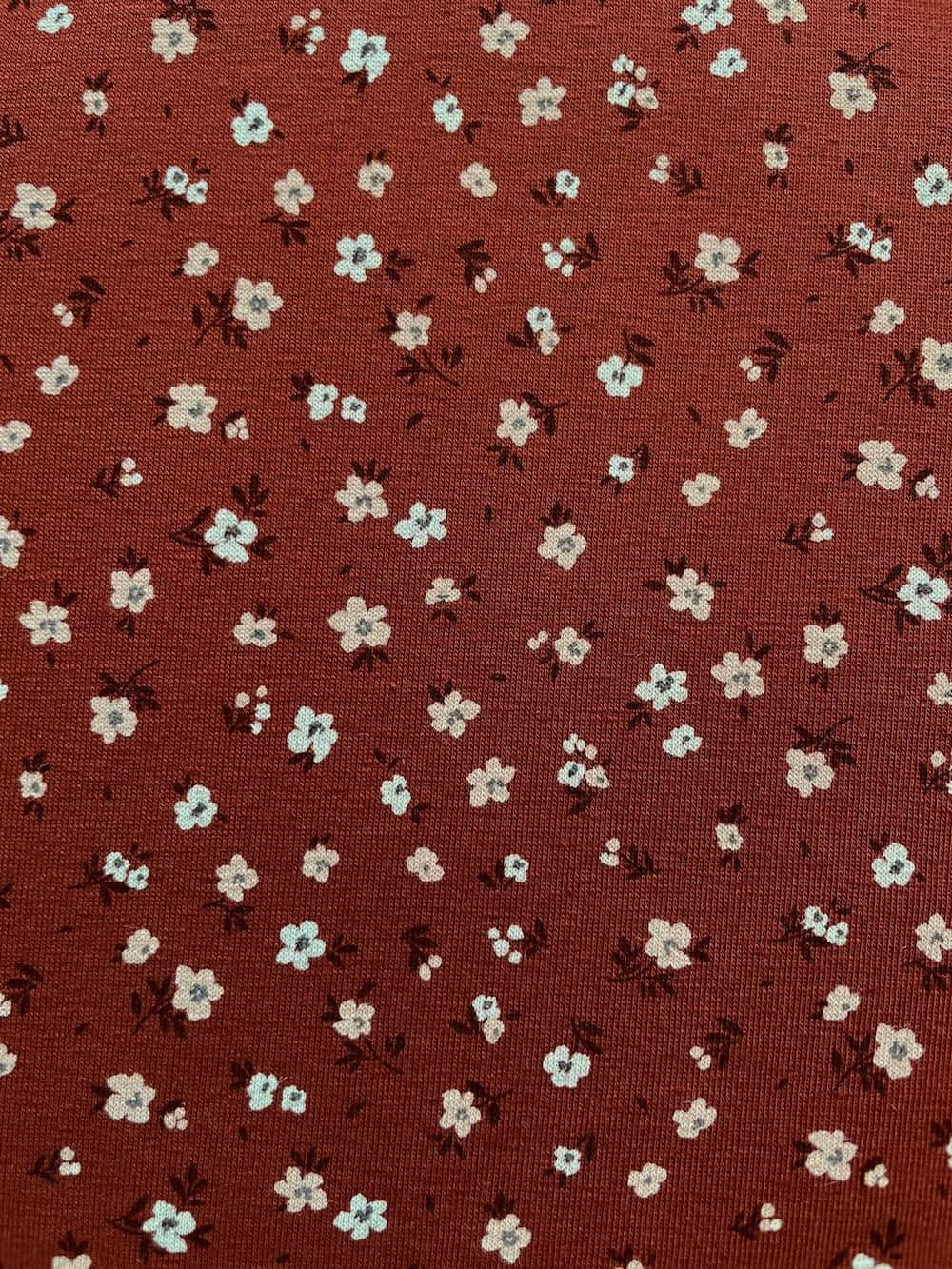 Weicher Jerseystoff in Rostbraun mit zierlichem weißen Blumenmuster, ideal für Kinderkleidung und Damenmode
