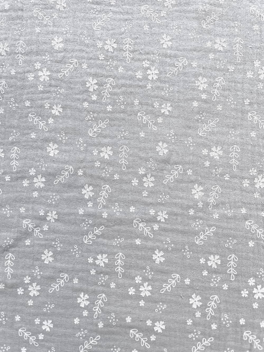 Hellgrauer Musselin-Stoff aus reiner Baumwolle mit feinen weißen Blüten und Zweigen, weiche Crinkle-Struktur für Bekleidung.