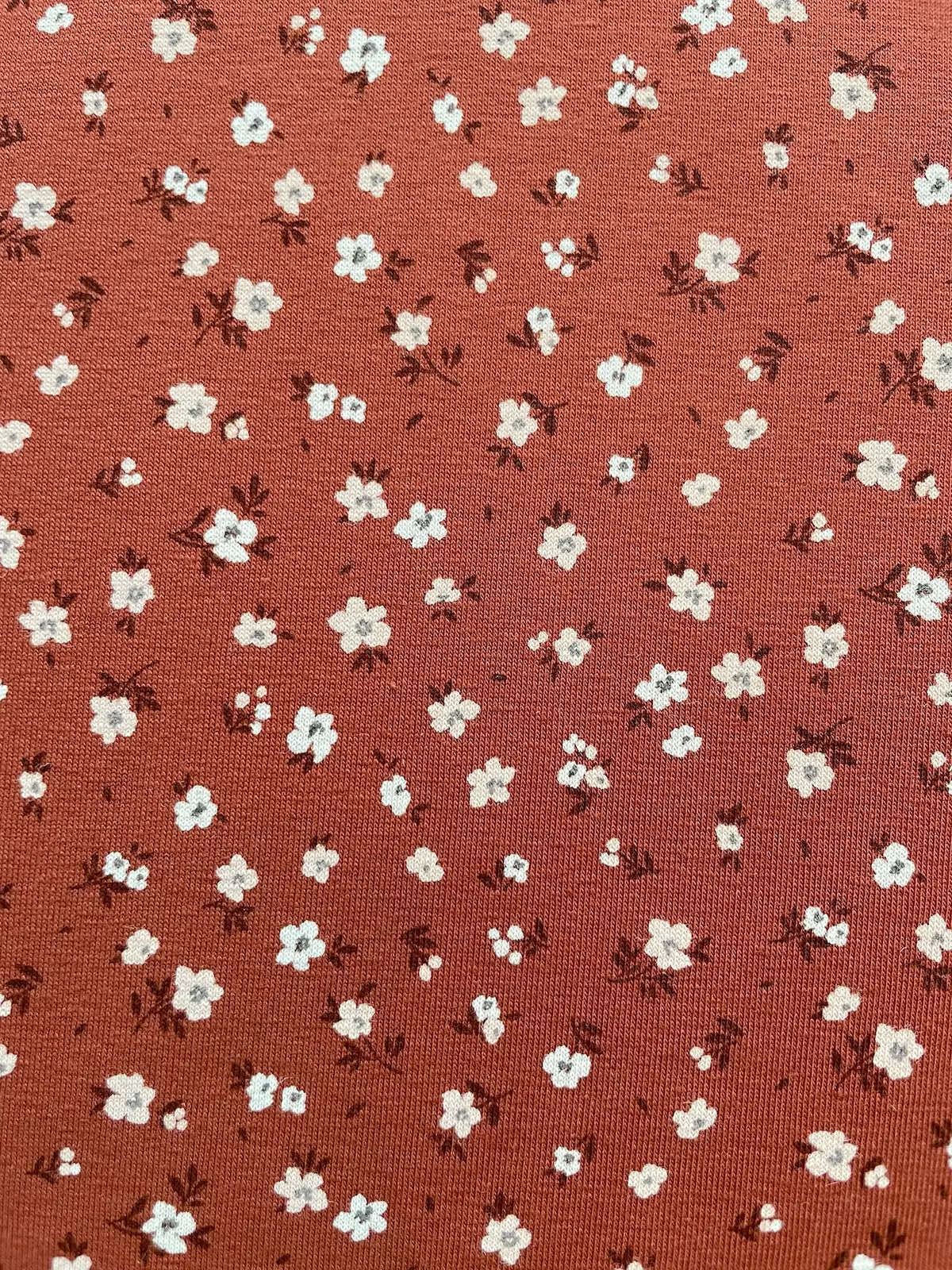 Weicher Jerseystoff in Rostbraun mit zierlichem weißen Blumenmuster, ideal für Kinderkleidung und Damenmode