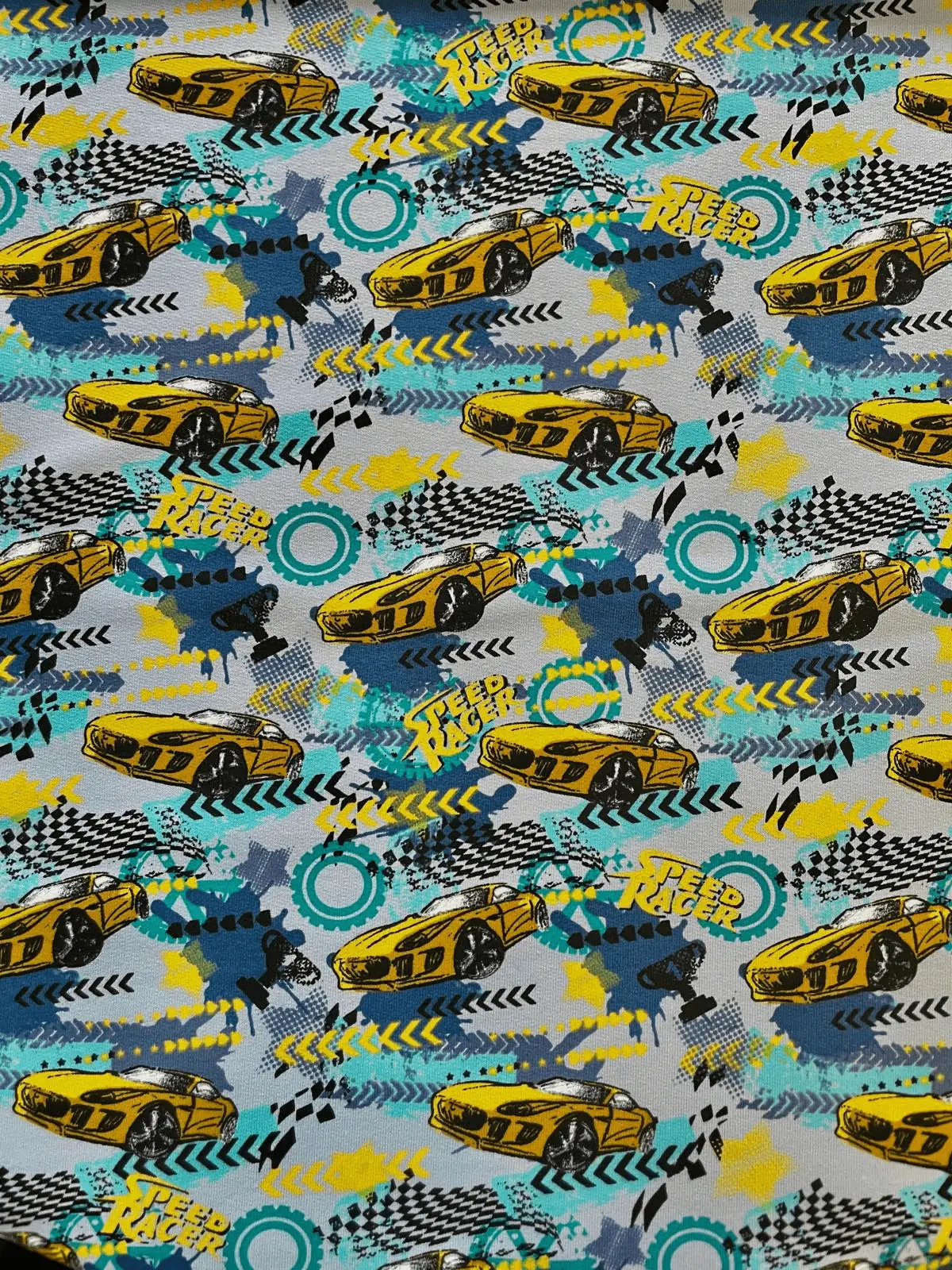 Elastischer French Terry Sommersweat-Stoff mit gelben Rennwagen, „Speed Racer“-Schriftzug und dynamischen Graffiti-Elementen auf blau-grauem Hintergrund.
