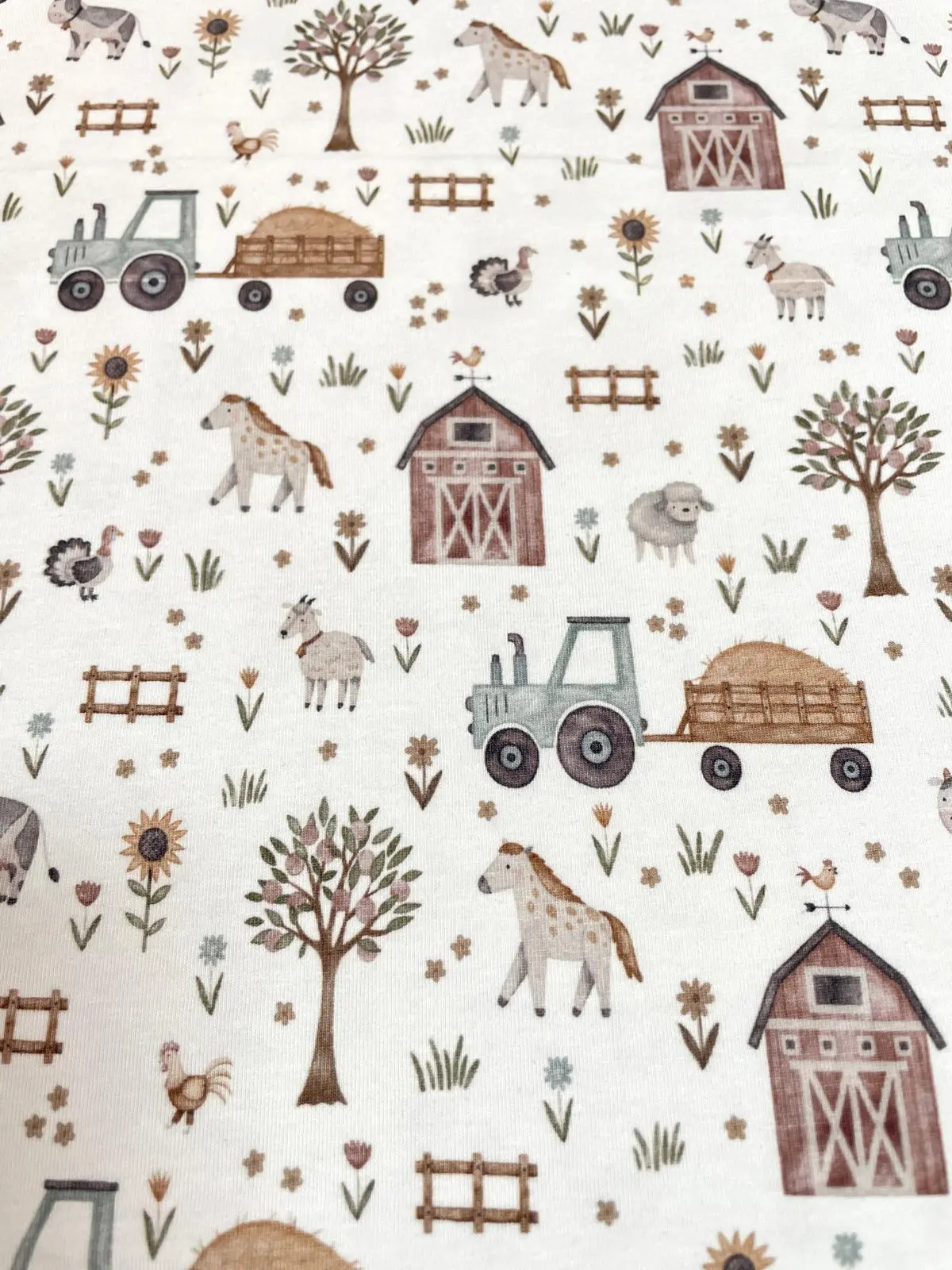 Weißer Jersey-Stoff mit detaillierten Bauernhof-Motiven im Aquarell-Stil: Traktor mit Heuanhänger, Scheune, Pferde, Ziegen, Schafe und Sonnenblumen.
