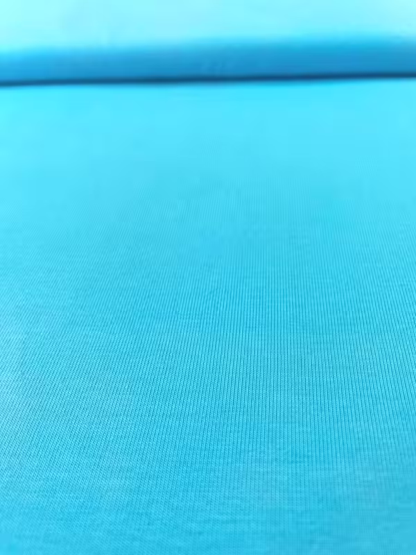 Nahaufnahme von elastischem Baumwolljersey in leuchtendem Türkis, glatte Oberfläche, 215g Gewicht, 144cm breite Meterware.