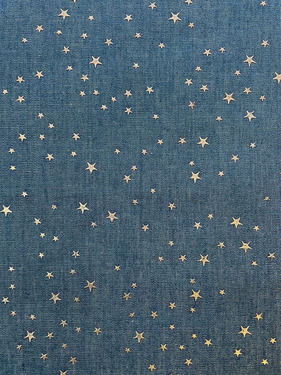 Nahaufnahme von jeansblauem Baumwollstoff mit fest aufgebrachten, silbernen Metall-Sternen. Die Sterne sind matt-glänzend ohne Glitzer, ideal für Kinderhosen und Schultüten.